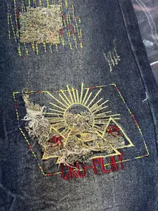 Close-up detail of retro distressed denim jeans with sun embroidery and patch design.