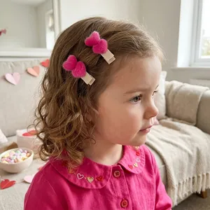 Ein junges Mädchen trägt niedliche rosa Samt-Herz-Haarspangen in einem Zimmer