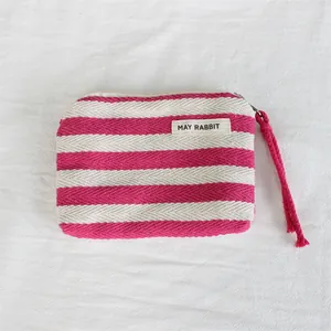 Close-up detail of a pink and white striped canvas coin purse with wrist strap and label