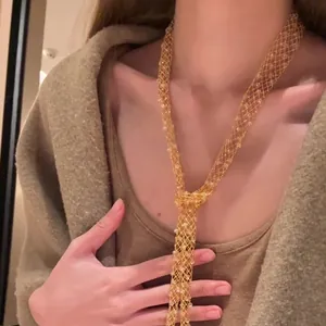 Close-up detail of a long gold-tone mesh necklace featuring embedded glass crystals.