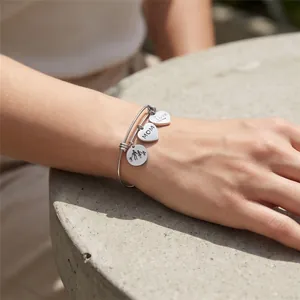 Close-up of adjustable stainless steel bangle with MOM and Love charms on wrist.