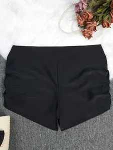Black high-waisted ruched swim shorts for women, flat lay view on decorative background