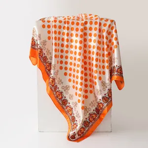 Elegant orange polka dot and paisley silk-like satin scarf draped on a stand.
