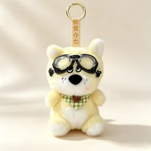 Detailed view of yellow plush dog keychain wearing black goggles and a green bandana