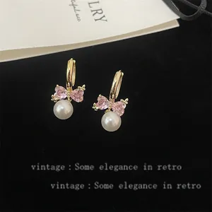 Macro view of vintage gold earrings featuring pink heart crystals and pearl drops.