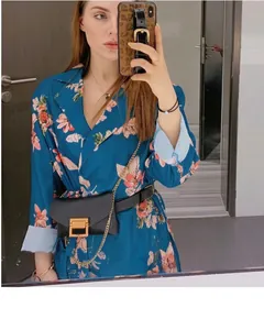 Minimalist black women's waist bag belt worn over a blue floral dress on model.