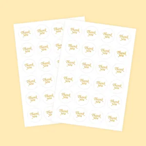 Two sheets of elegant gold foil Thank You round stickers on a soft pale yellow background