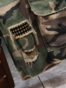 Close-up of distressed camouflage cargo shorts with golden studs and frayed edges.