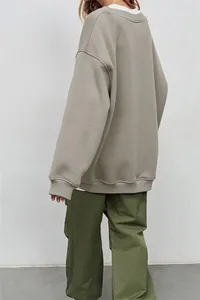 Vista posteriore di una felpa beige oversize minimalista da donna con pantaloni verdi