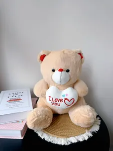 Close-up detail of a soft beige teddy bear holding a white I Love YOU embroidered heart plush