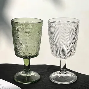 Gros plan de verres à pied vintage en relief français avec motifs de feuilles verts et clairs.