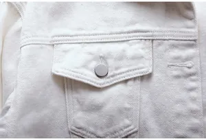 Detalle de primer plano del bolsillo y el botón de plata de una chaqueta vaquera blanca.