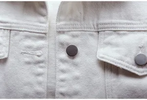 Primer plano de botones metálicos mate y textura de mezclilla en una chaqueta blanca