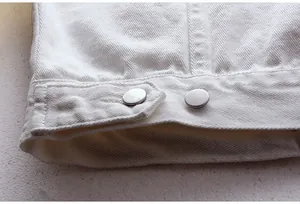 Vista detallada del dobladillo de una chaqueta vaquera blanca con botones metálicos