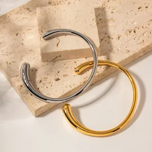 Dettaglio di bracciali aperti lucidi in oro e argento su sfondo di pietra ruvida