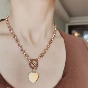 Détail d'un collier pendentif cœur en or rose avec fermoir OT porté au cou d'une femme