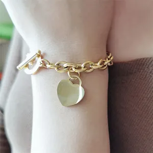 Gros plan d'un bracelet à breloque cœur en acier doré avec fermoir à bascule au poignet
