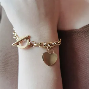 Gros plan d'un bracelet en acier doré avec pendentif cœur et fermoir T