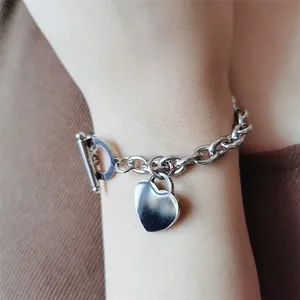 Gros plan d'un bracelet en acier inoxydable avec pendentif cœur et fermoir en T au poignet.
