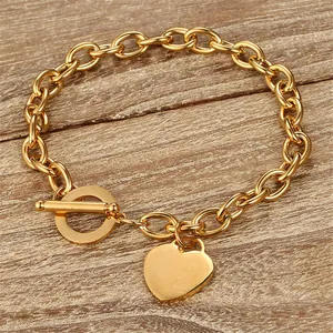 Détail d'un bracelet doré en acier inoxydable avec pendentif cœur et fermoir T sur bois.