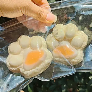 Cute cat paw squishy toy in creamy white and orange, shown in a clear plastic tray.