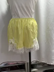 Dettaglio di pantaloncini larghi in raso giallo chiaro con bordo in pizzo bianco.