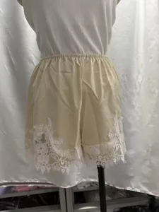 Vista dettagliata dei pantaloncini in raso champagne con elegante pizzo floreale bianco