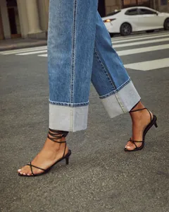 Detail view of cuffed straight-leg denim jeans paired with black strappy sandals on street.
