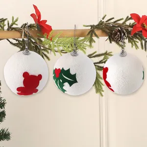 Dettaglio di palline di Natale in schiuma bianca con disegni di orsetti e foglie di agrifoglio.