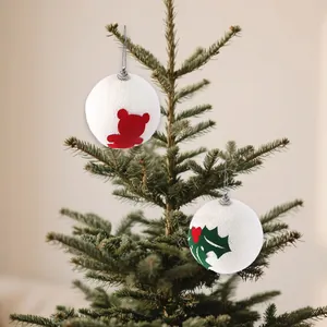 Dettaglio di palline di Natale in schiuma bianca con motivi orso e agrifoglio su albero.