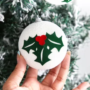 Primo piano di palla di Natale in schiuma bianca con foglie di agrifoglio verdi e bacche rosse
