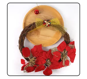 Detail of a Christmas wreath with red poinsettia and golden bow on wooden plate.