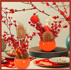 Detailansicht von zwei festlichen orangefarbenen Kakipöpfen mit roten Beeren und Golddeko.