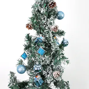Beflockter Weihnachtsbaum mit blauen Ornamenten, Minigeschenken und natürlichen Tannenzapfen.