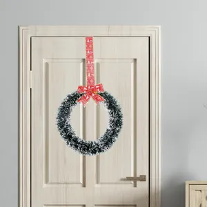 Green Christmas tinsel wreath with red patterned bow hanging on a white door