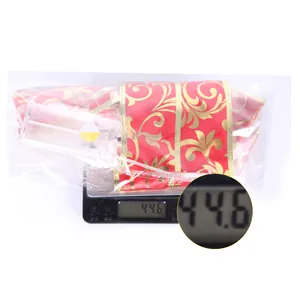Lighted red and gold Christmas bow ornament showing a weight of 44.6g on a scale