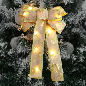 Warm LED glowing Christmas bow with gold trim and reindeer pattern on a snowy tree