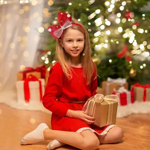 Child wearing a festive red Christmas bow headband with sparkles in a warm holiday setting