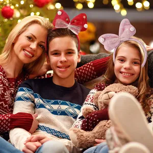 Family wearing festive Christmas bow headbands in front of a glowing holiday tree