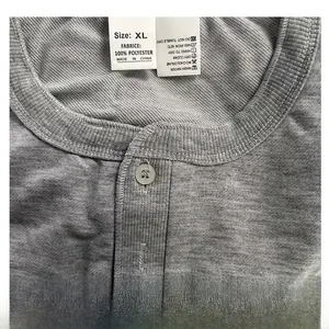 Detailaufnahme des Waschetiketts aus 100 % Polyester und der Stoffstruktur eines grauen Henley-Shirts