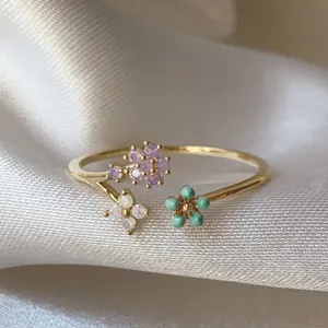 Primo piano di anello regolabile in oro con fiori di zircone e perline turchesi.