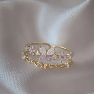 Dettaglio di eleganti anelli regolabili in oro con farfalla e fiori in zircone viola