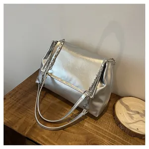 Detailed view of a silver metallic shoulder bag with chain straps on a wooden surface.