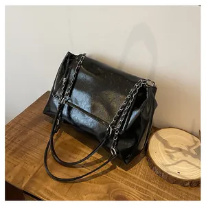 Detailed view of a black glossy leather underarm bag with silver chain on a wood surface.