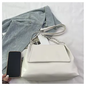 Detail view of a minimalist white leather shoulder bag with chain strap and denim jacket