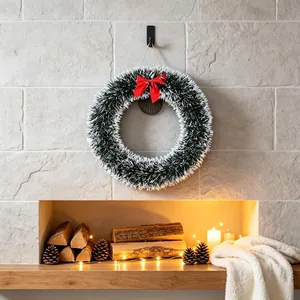 Classic Christmas wreath with white-green tinsel and red bow hanging over a fireplace