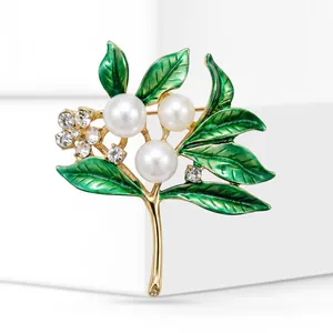 Close-up detail of elegant gold-tone branch brooch with green enamel leaves and pearls.