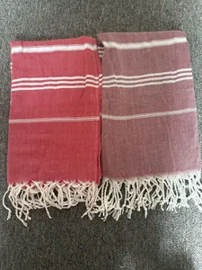 Detailed view of two striped Turkish cotton beach towels with white tassels in red and burgundy.