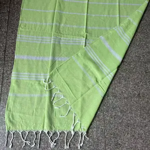 Detail of a lime green Turkish beach towel with white stripes and hand-tied tassels.