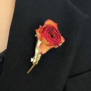 Close-up of a realistic dried rose brooch with gold-toned stem on black fabric